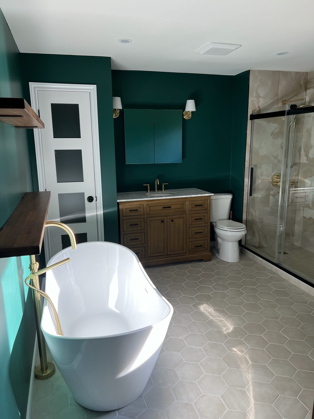 Finished bathroom with green walls, freestanding tub and glass shower