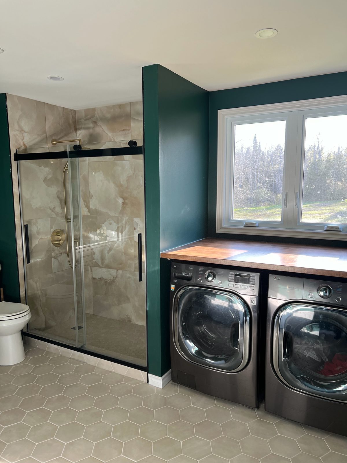 Finished laundry with butcher block counter over washer and dryer, next to glass shower